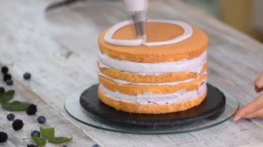 Pastry chef is squeezing the whipped cream on the cake.