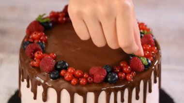 Pastry chef decorating berry cake with a mint leaves.
