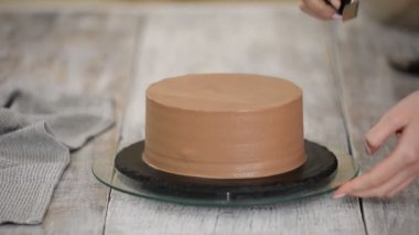 Genç kadın çikolatalı keki süslüyor, ev mutfağında duruyor. Kadın çikolatalı keki bitiriyor..