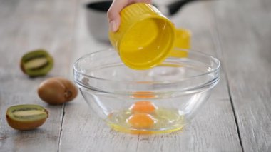 Aşçı, karıştırıcı kullanarak, tavuk yumurtalarını cam bir kaseye döker, aynı zamanda bir kaseye şeker döker ve yumurtaları çırpmaya devam eder..