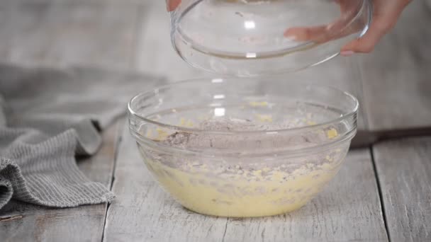 Ajouter la farine à la pâte. Les mains du chef plient les ingrédients secs à la pâte dans un bol . — Video