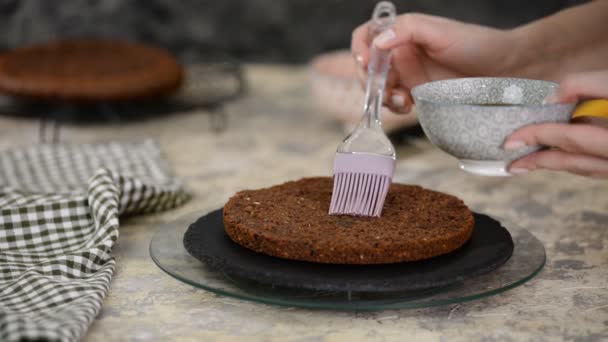 Onherkenbare vrouwelijke banketbakker dompelt spons cake met zoete koffie met behulp van silicium koken borstel in de keuken, close-up. — Stockvideo