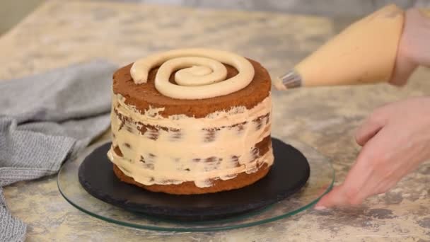 Una chica haciendo un pastel en una panadería. Baker aprieta crema sobre una capa de pastel . — Vídeos de Stock