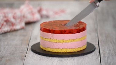 Dişi eller ahududulu krema ve jöle katmanlı tatlı pasta kesiyor..