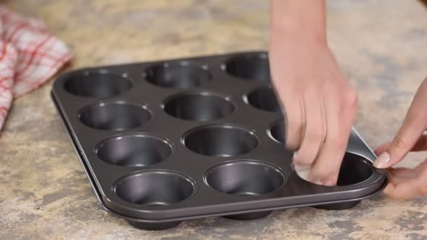 Mujer esparciendo aceite en moldes de magdalenas para hacer deliciosos cupcakes, magdalenas. Pasteles caseros . — Vídeo de stock