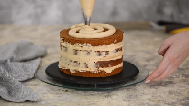 Una chica haciendo un pastel en una panadería. Baker aprieta crema sobre una capa de pastel . — Vídeo de stock