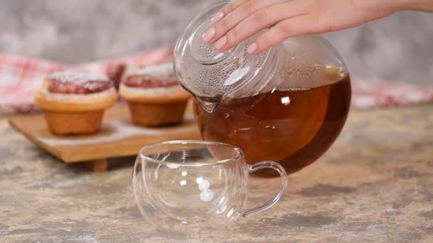 Verser le thé chaud dans une tasse en verre. Une tasse de thé avec des petits pains aux roses, des petits pains sucrés avec de la poudre de sucre . — Video