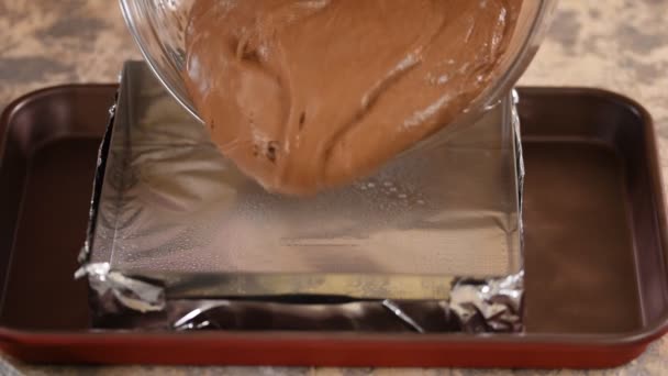 Ein Koch in der Küche gießt Schokoladenkuchenteig in eine quadratische Backform, um zum Dessert in den Ofen zu gehen.