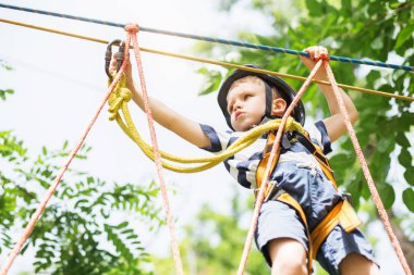 Kids climbing in adventure park. Boy enjoys climbing in the rope clipart