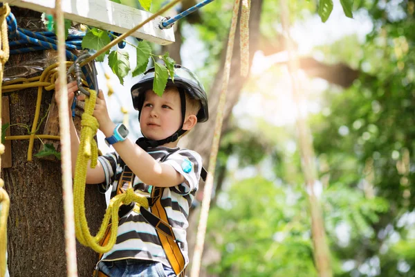 Barnen klättrar i äventyrsparken. Pojke har klättring i repet — Stockfoto