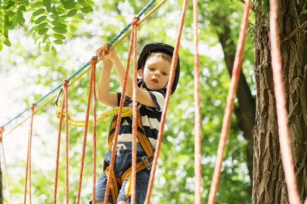 Barnen klättrar i äventyrsparken. Pojke har klättring i repet — Stockfoto