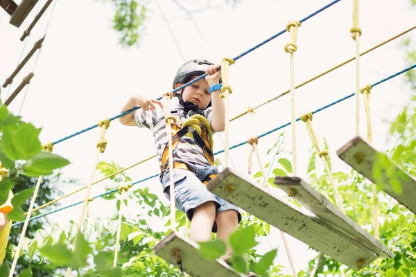 Barnen klättrar i äventyrsparken. Pojke har klättring i repet — Stockfoto