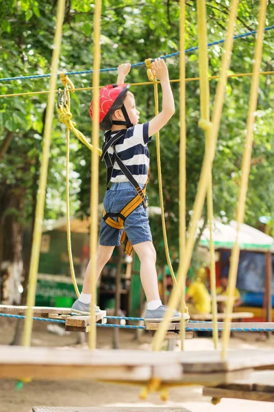 Crianças escalando no parque de aventuras. Rapaz gosta de escalar na corda — Fotografia de Stock