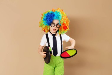 Blithesome çocuklar. Büyük neon giymiş mutlu palyaço çocuk portresi peruk renkli. Palyaço peruk ve gözlük catch topu oyun oynayan çocuk