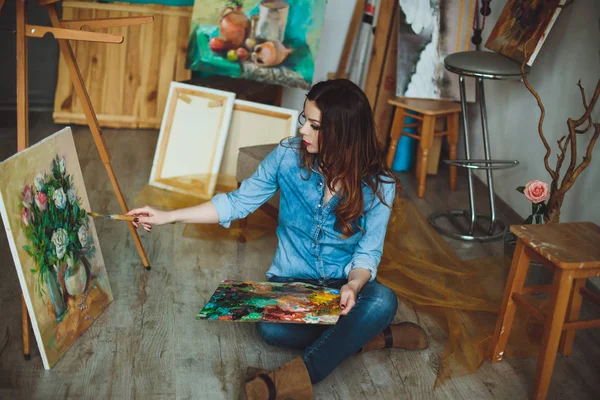 Woman artist painting a picture in a studio. Creative pensive painter girl paints a colorful picture on canvas with oil colors in workshop.