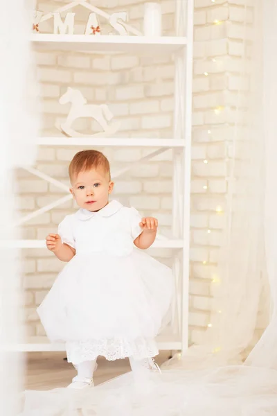 Beautiful baby girl in a white dress in the interior with Christ — Stock Photo, Image