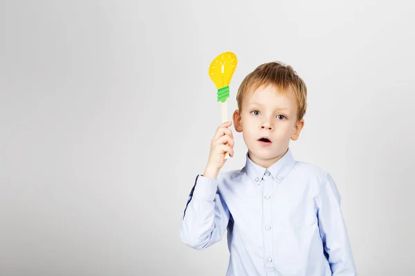 Cute boy with yellow paper lightbulb against a white background. — Stock Photo, Image