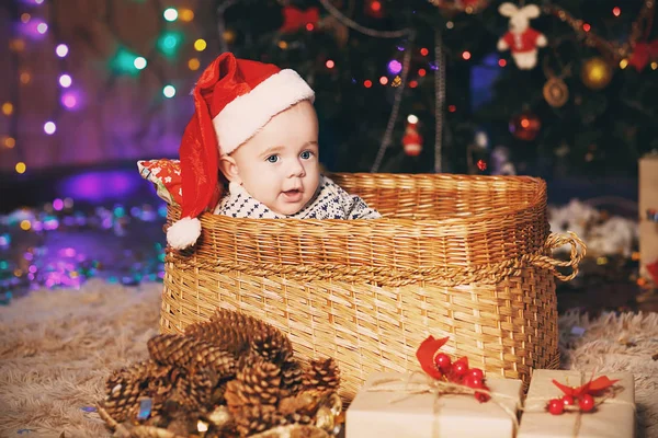 Mały chłopiec dziecko w Santa hat siedzi w wiklinowym koszu. — Zdjęcie stockowe