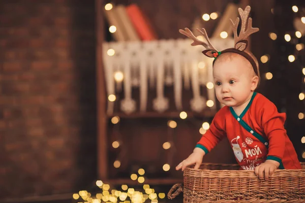 Baby jongetje in rendieren geweien zitten in een rieten mand. — Stockfoto