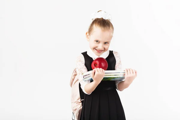 微笑的小女孩与持有书籍和大红苹果在白色背景下的大背包 看着照相机 学校的概念 回到学校 — 图库照片