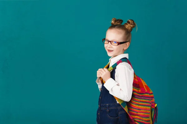 Zabawny uśmiechający się mała dziewczynka z f skoki i o plecak duży — Zdjęcie stockowe