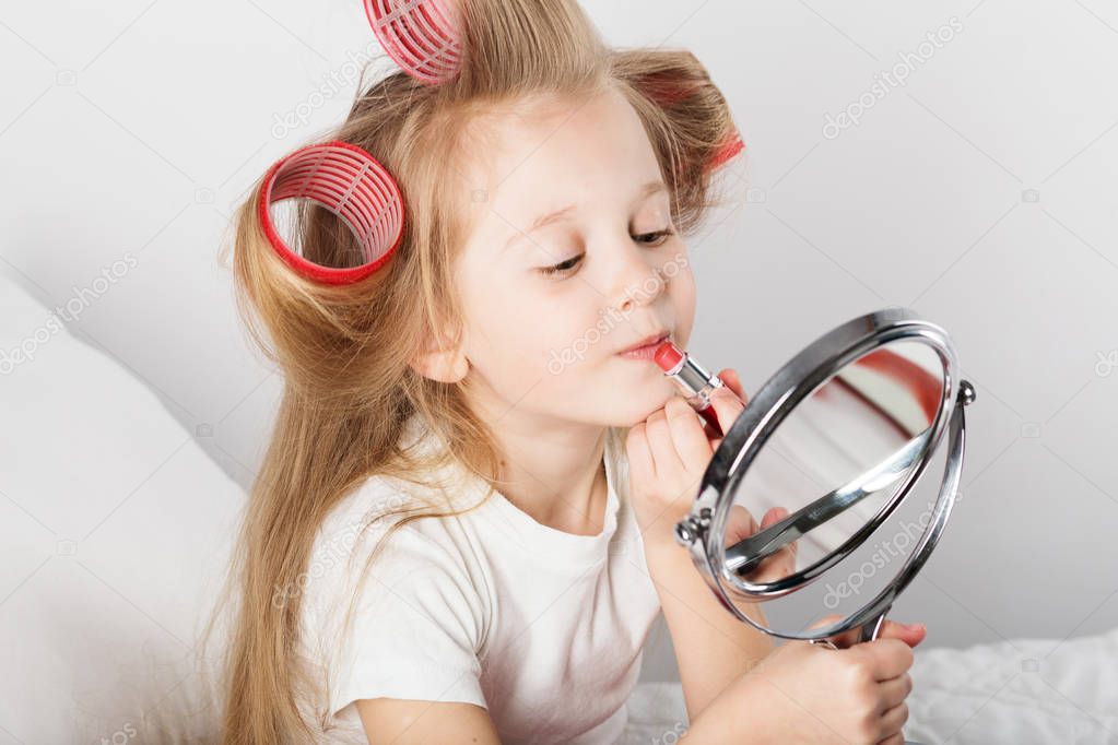 Beautiful little lady with curlers on her head looking at mirror