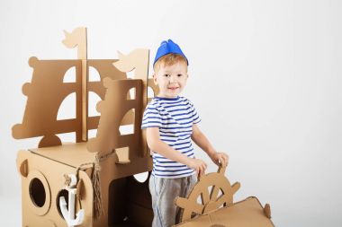 Küçük çocuk beyaz zemin üzerine karton gemi ile oynarken