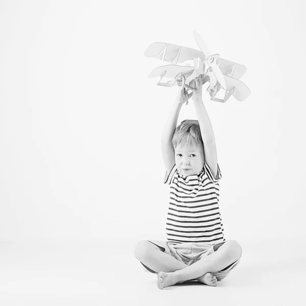 Menino brincando com papel brinquedo avião sentado no chão um — Fotografia de Stock