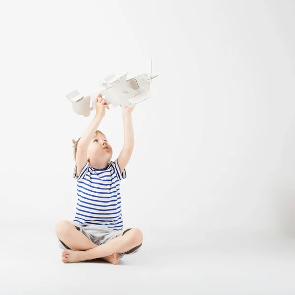 Niño jugando con papel juguete avión sentado en el suelo a — Foto de Stock