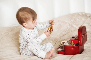 Bir yatakta oturup annesinin takı ile oynayan kız bebek 