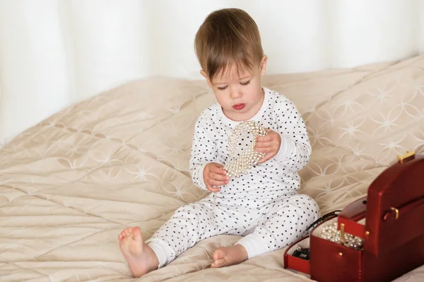 Κοριτσάκι παίζει με τα κοσμήματα της μητέρας κάθεται σε ένα κρεβάτι σε — Φωτογραφία Αρχείου