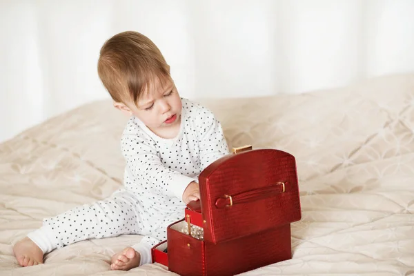Bambina che gioca con i gioielli di sua madre seduta su un letto in — Foto Stock