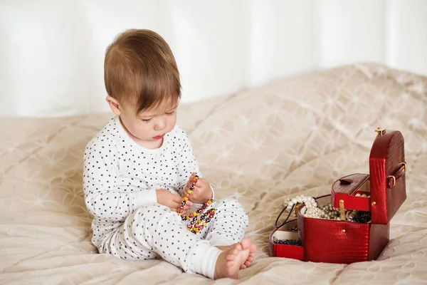 Menina bebê brincando com jóias de sua mãe sentado em uma cama em — Fotografia de Stock