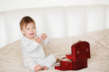 Bir yatakta oturup annesinin takı ile oynayan kız bebek 