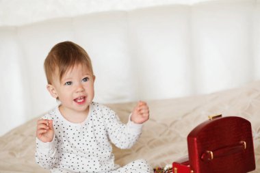 Bir yatakta oturup annesinin takı ile oynayan kız bebek 