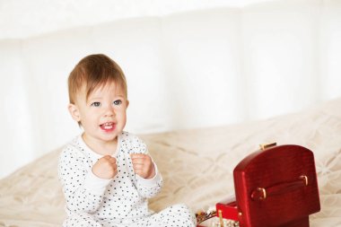 Bir yatakta oturup annesinin takı ile oynayan kız bebek 