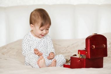 Bir yatakta oturup annesinin takı ile oynayan kız bebek 