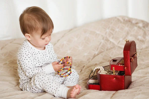 Menina bebê brincando com jóias de sua mãe sentado em uma cama em — Fotografia de Stock