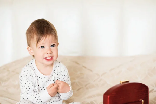 Baby girl playing with her mother's jewelry sitting on a bed in — Stock Photo, Image