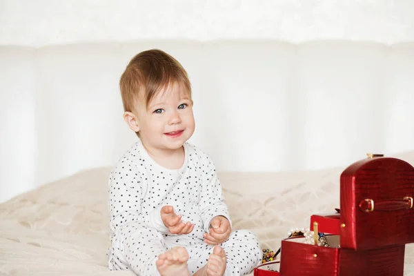 Baby flicka som leker med hennes mors smycken sitter på en säng i — Stockfoto