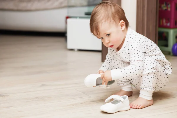 Linda niña en pijama en cuclillas en el suelo trata de poner en su — Foto de Stock