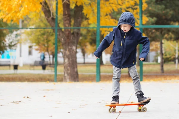 Little urban boy with a penny skateboard. Kid skating in an autu — Stock Photo, Image