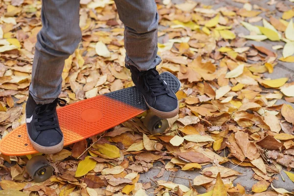 Menino de pé em um skate laranja ao ar livre. Fechar ima — Fotografia de Stock