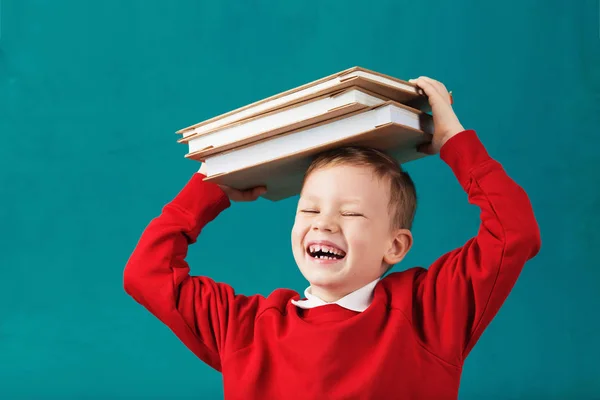 Glada leende liten skola pojke med stora böcker på hans huvud ha — Stockfoto