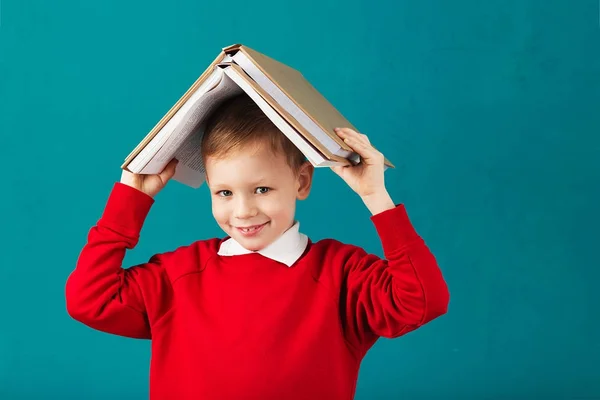 Wesoły, uśmiechnięty chłopczyk szkoły z duże książki na głowie ha — Zdjęcie stockowe
