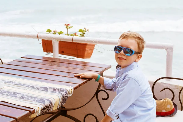 Boy in restaurant on sea beach, no one else, white chairs and st — Stock Photo, Image