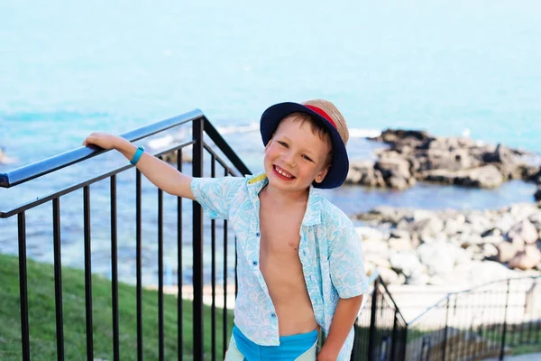 Niño pequeño en camisa y pantalones cortos en la arena de la playa. Pequeño niño tiene —  Fotos de Stock