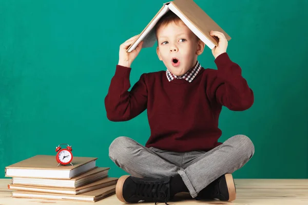 Cheerful smiling little school boy with big heavy books on his h — Stock Photo, Image