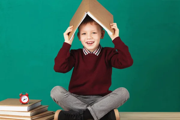 Cheerful smiling little school boy with big heavy books on his h — Stock Photo, Image