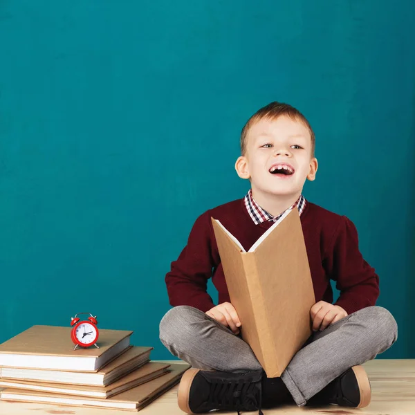 Cheerful smiling little school boy sitting on a desk against tur — Stock Photo, Image